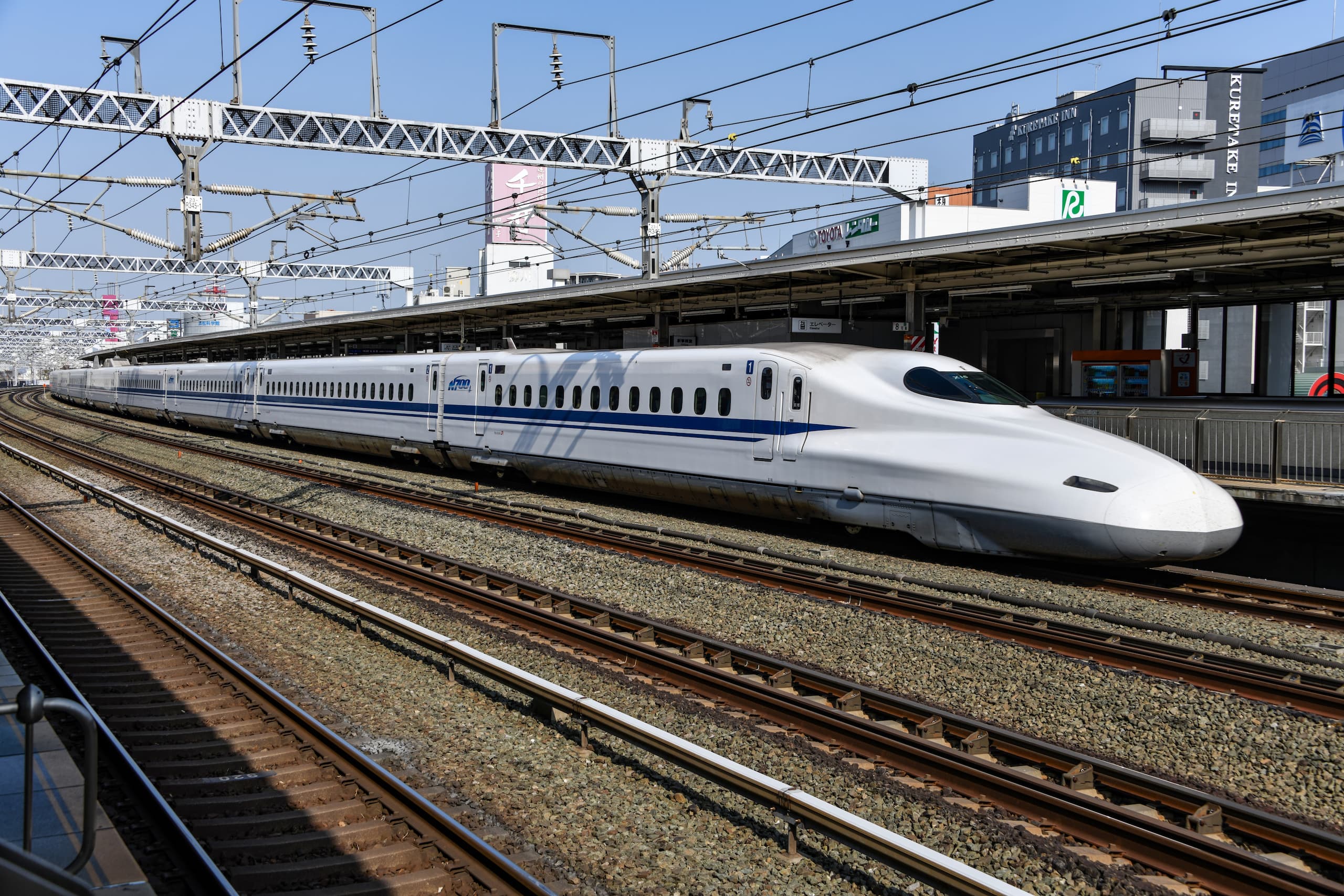 White and blue Japanese bullet train speeding by a train station.